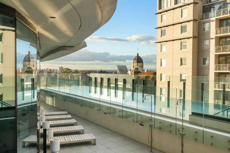An infinity pool on a terrace with lounge chairs overlooking a city skyline