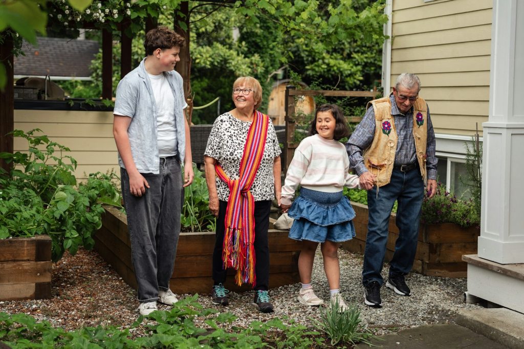 A family of four walking together in a garden beside a house