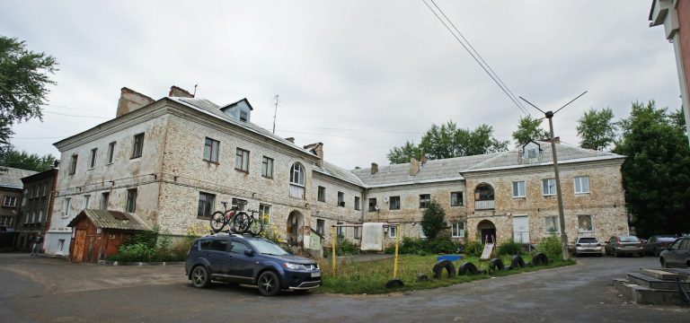 A dark blue SUV with bicycles on the roof parked before old brick buildings