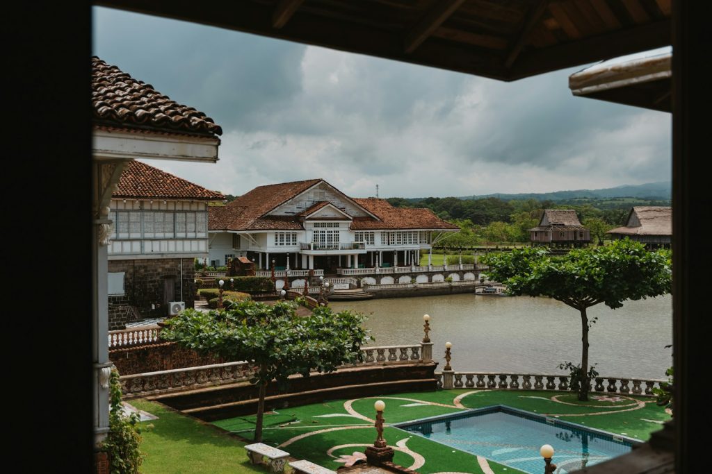 A colonial style mansion with a tiled roof overlooking a river and pool